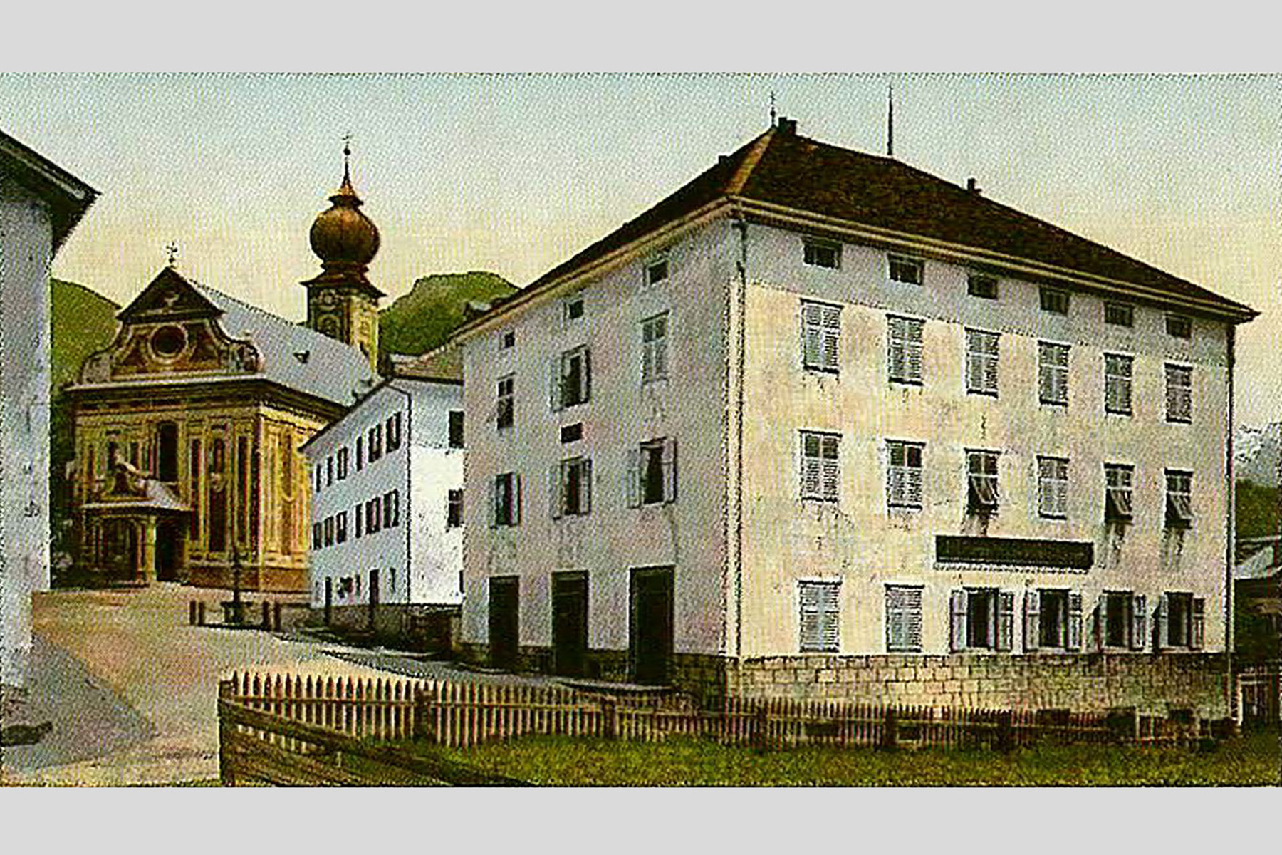 Haus Purger und ehemaliges Gemeinde- und Arzthaus vor der Pfarrkirche. Kolorierte Postkarte um 1900