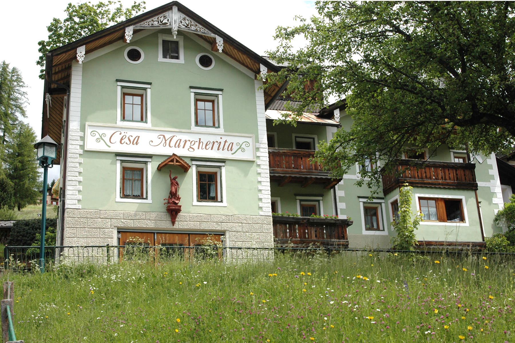 Frühlinghaftes Foto der Villa Margherita in heutigen Zeiten. Gut sichtbar die Inschrift „Cësa Margherita“ und die Marienstatue.