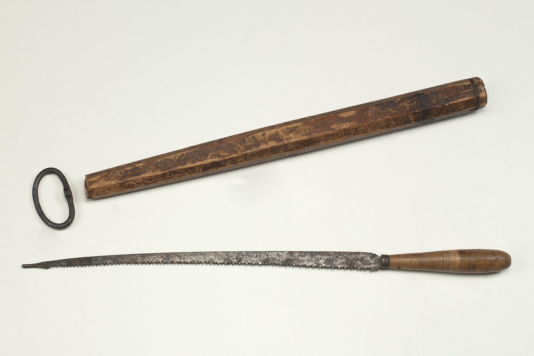 Eisensäge mit gedrechseltem Holzgriff und dazugehöriger Holzscheide sowie Eisenring zum Fixieren der Säge.