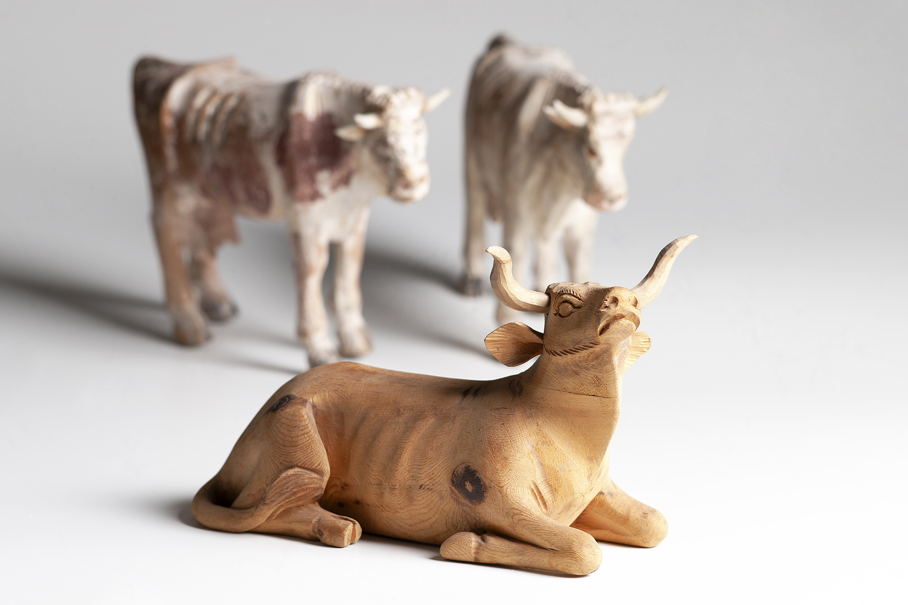 Drei geschnitzte Holztiere aus Villnöß, eine naturbelassene liegende Kuh und zwei bemalte stehende Kühe 