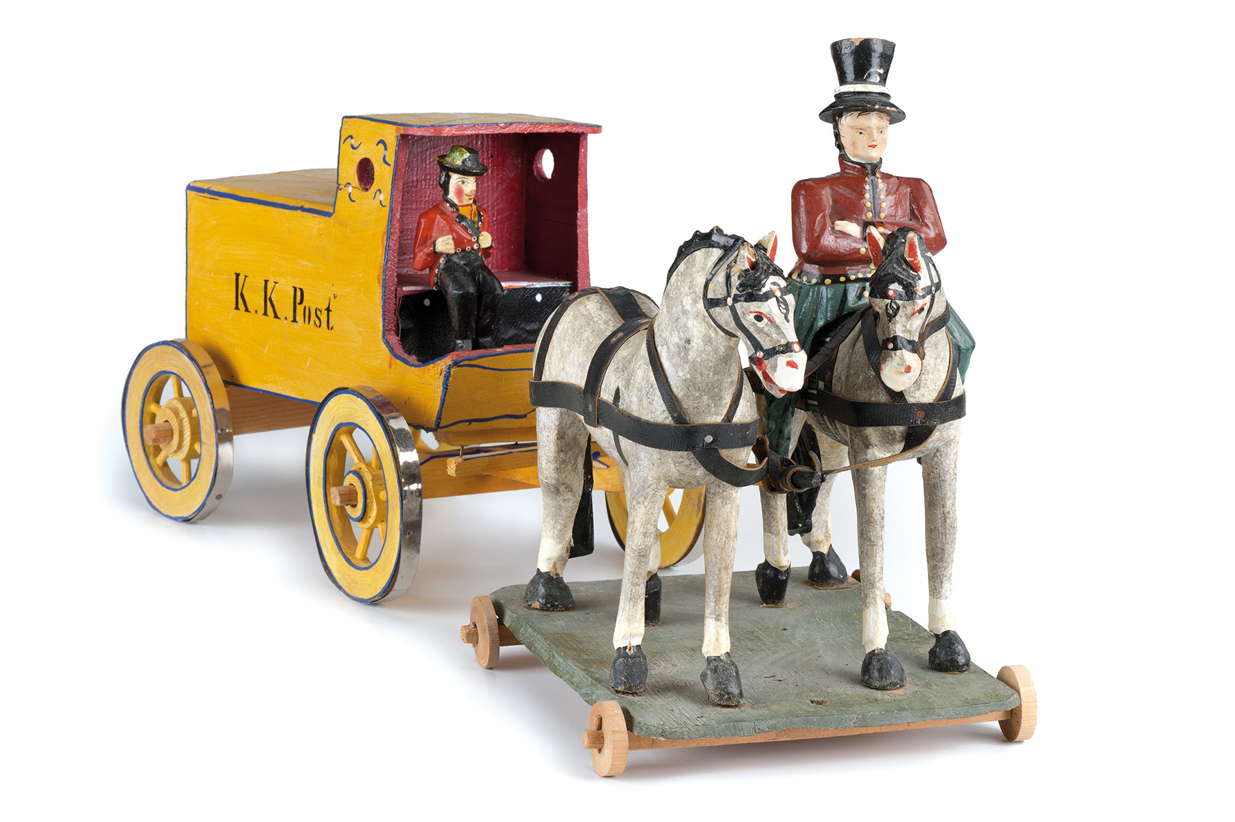 Bemalte Postkutsche aus Holz mit der Aufschrift „K. K. Post“, die von einem Pferdegespann auf Räderbrett gezogen wird