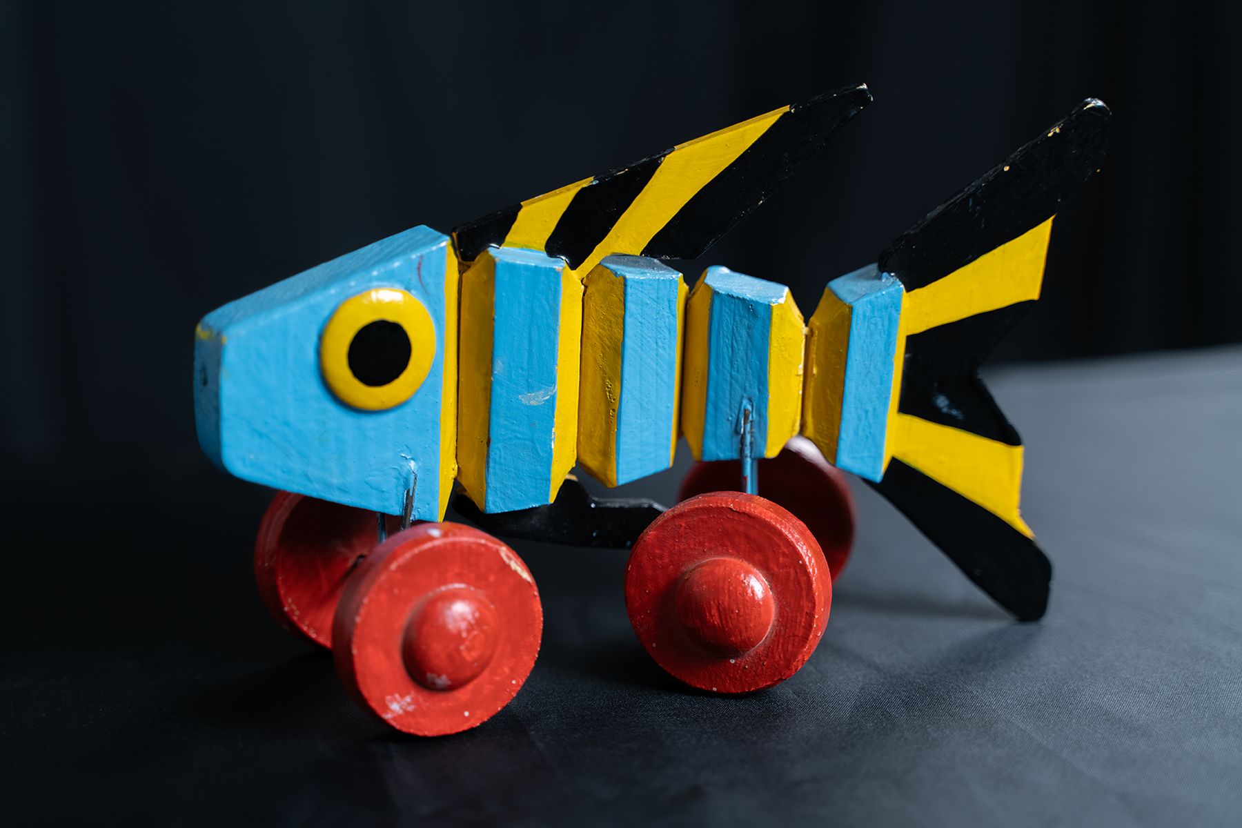 Hölzerner, blau-gelb bemalter Fisch auf vier roten Rädern