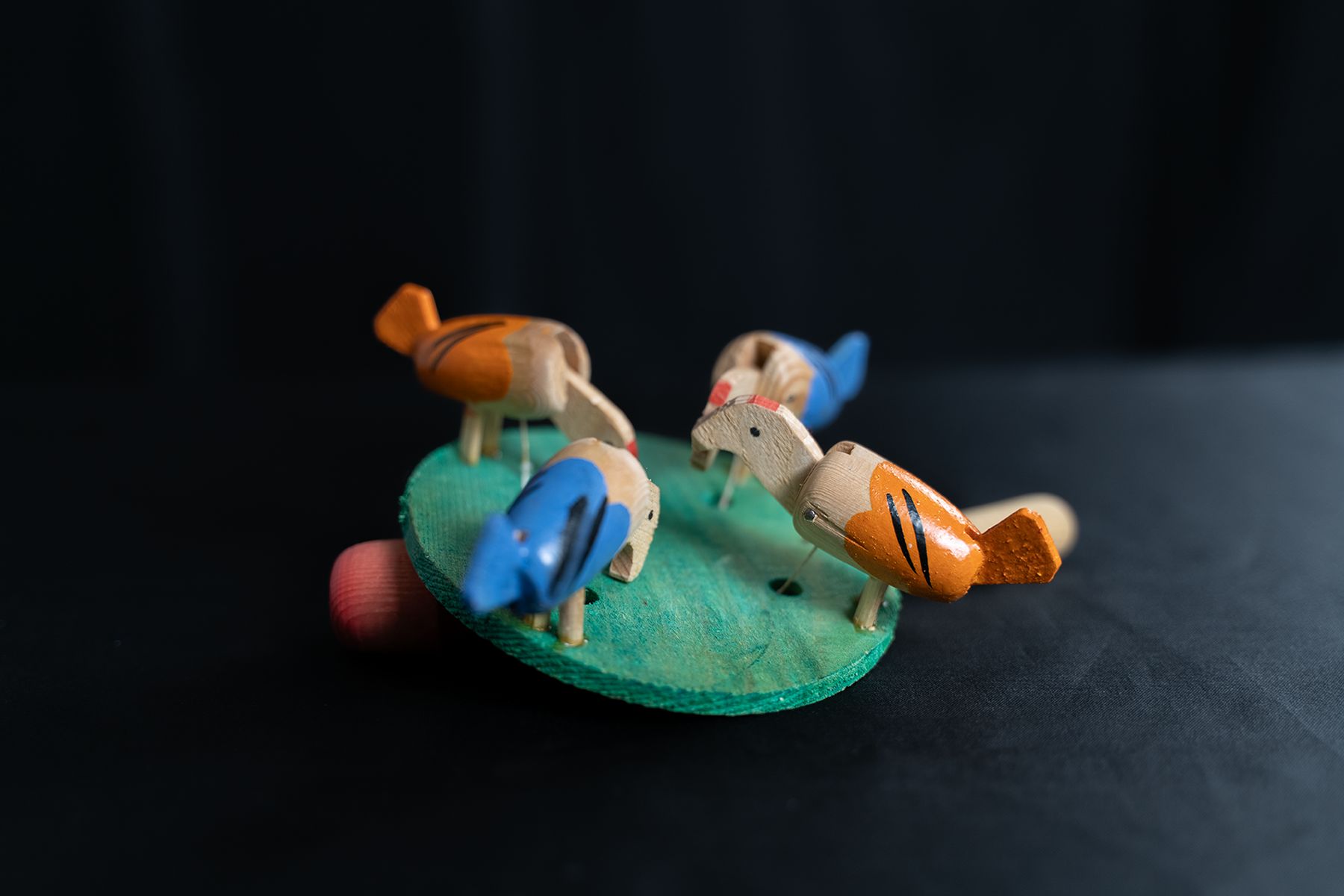 Vier pickende Hühner, mit den Köpfen zueinander gedreht, auf einem runden Brett, an dem ein Pendel befestigt ist