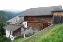 An den Steilhang angepasster Hof von Ulëta, das Wirtschaftsgebäude aus Holz hinter dem gemauerten Wohnhaus