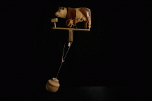 Das Pendel bewegt die Köpfe der Figuren des hölzernen Spielzeugs; dann trinkt die Kuh aus dem Trog und das Kälbchen am Euter der Kuh. 
