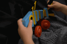 Hölzerner, mehrfarbig bemalter Fisch auf vier Rädern, der aus fünf miteinander verbundenen, beweglichen Teilen besteht