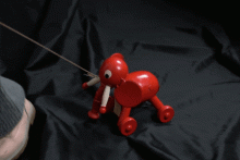 Hölzerner, rot bemalter Elefant auf vier Rädern, der beim Nachziehen den Kopf seitlich nach links und rechts bewegt 