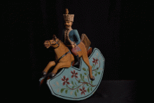 Holzspielzeug eines Reiters in Uniform auf einer Wiege, die beim Anstoßen vor und zurück wippt